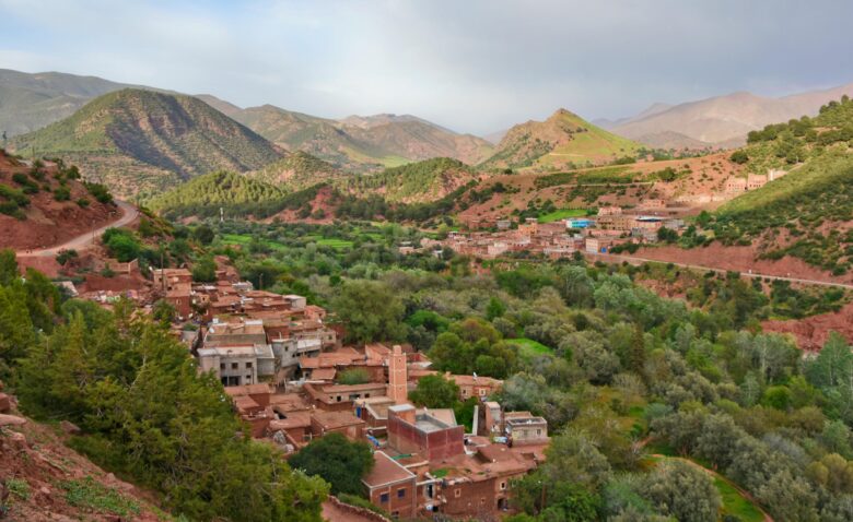 Breathtaking panoramic view of the Moroccan Atlas Mountains and a traditional Berber village nestled in a valley, representing an authentic cultural and natural escape for excursions from Marrakech, perfect for hiking and photography.